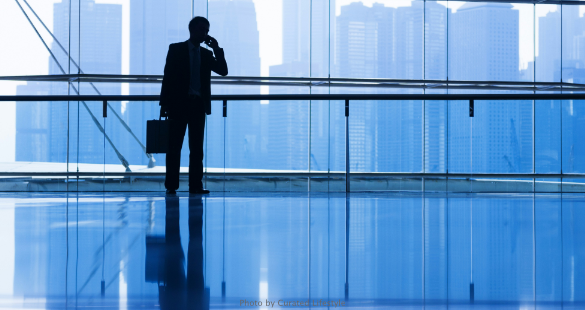 Business professional using a mobile phone beside a reflective office building.
