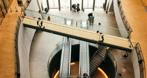 People moving through intersecting walkways inside a modern business building.