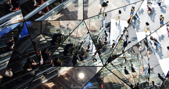 People and their reflections moving through a modern glass building.